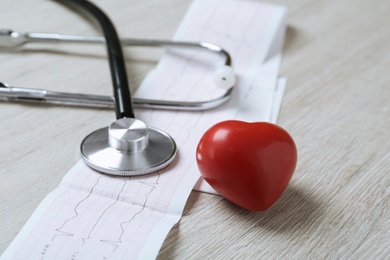 Photo of Cardiogram report, red heart and stethoscope on wooden table, closeup