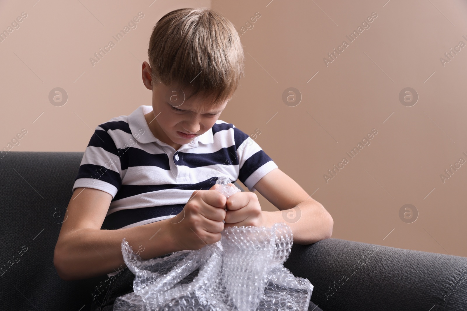 Photo of Angry boy popping bubble wrap indoors. Stress relief