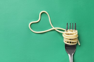 Photo of Heart made of tasty spaghetti and fork on green background, top view