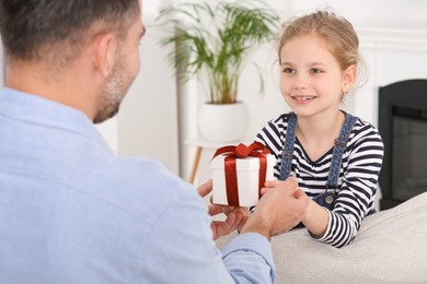 Photo of Cute little girl presenting her father with gift at home