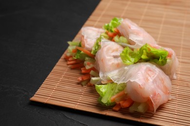 Tasty spring rolls and bamboo mat on black textured table, closeup. Space for text