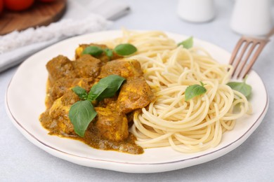 Photo of Delicious chicken, pasta with curry sauce and basil served on white table, closeup