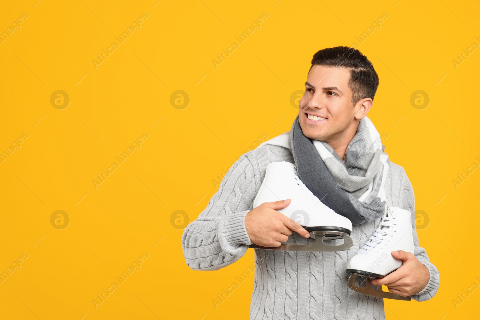 Photo of Happy man with ice skates on yellow background. Space for text