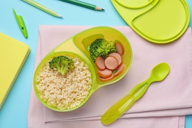 Photo of Bowl with tasty pasta, broccoli and sausage on light blue background, flat lay
