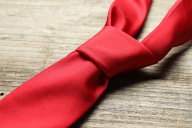 Photo of One red necktie on light wooden table, closeup