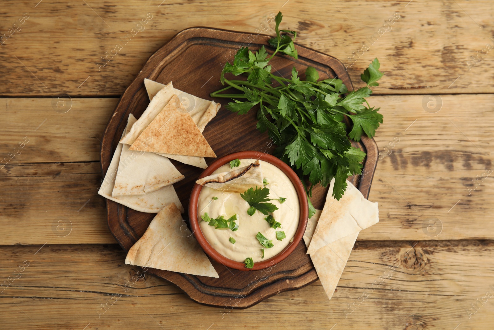 Photo of Delicious hummus with pita chips and parsley on wooden table, top view