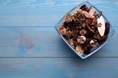 Photo of Aromatic potpourri of dried flowers in glass bowl on light blue wooden table, top view. Space for text
