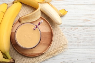 Glass of tasty banana smoothie with straw and fresh fruits on white wooden table, flat lay. Space for text