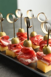 Tasty canapes with olives, prosciutto and cheese on grey table, closeup