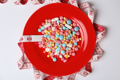 Photo of Plate with weight loss pills and measuring tape on white background, top view