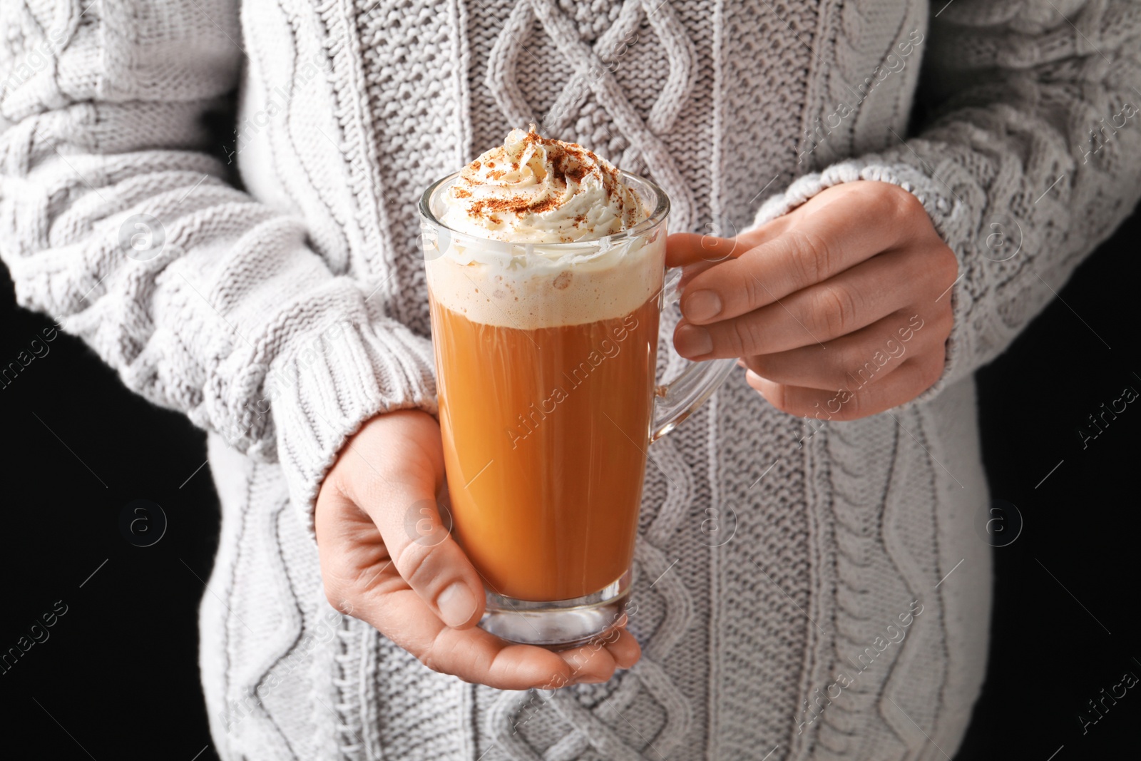 Photo of Woman holding glass cup with tasty pumpkin spice latte on black background, closeup