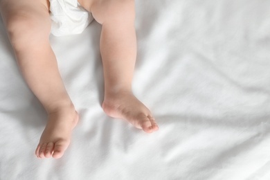 Photo of Little baby with cute feet on bed sheet, above view. Space for text