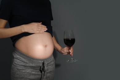 Photo of Pregnant woman with glass of red wine on dark background, space for text. Alcohol addiction