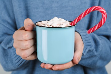 Photo of Woman holding cup of delicious hot chocolate with marshmallows and candy cane, closeup