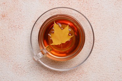Photo of Cup of tasty tea and autumn yellow leaf on color background, top view