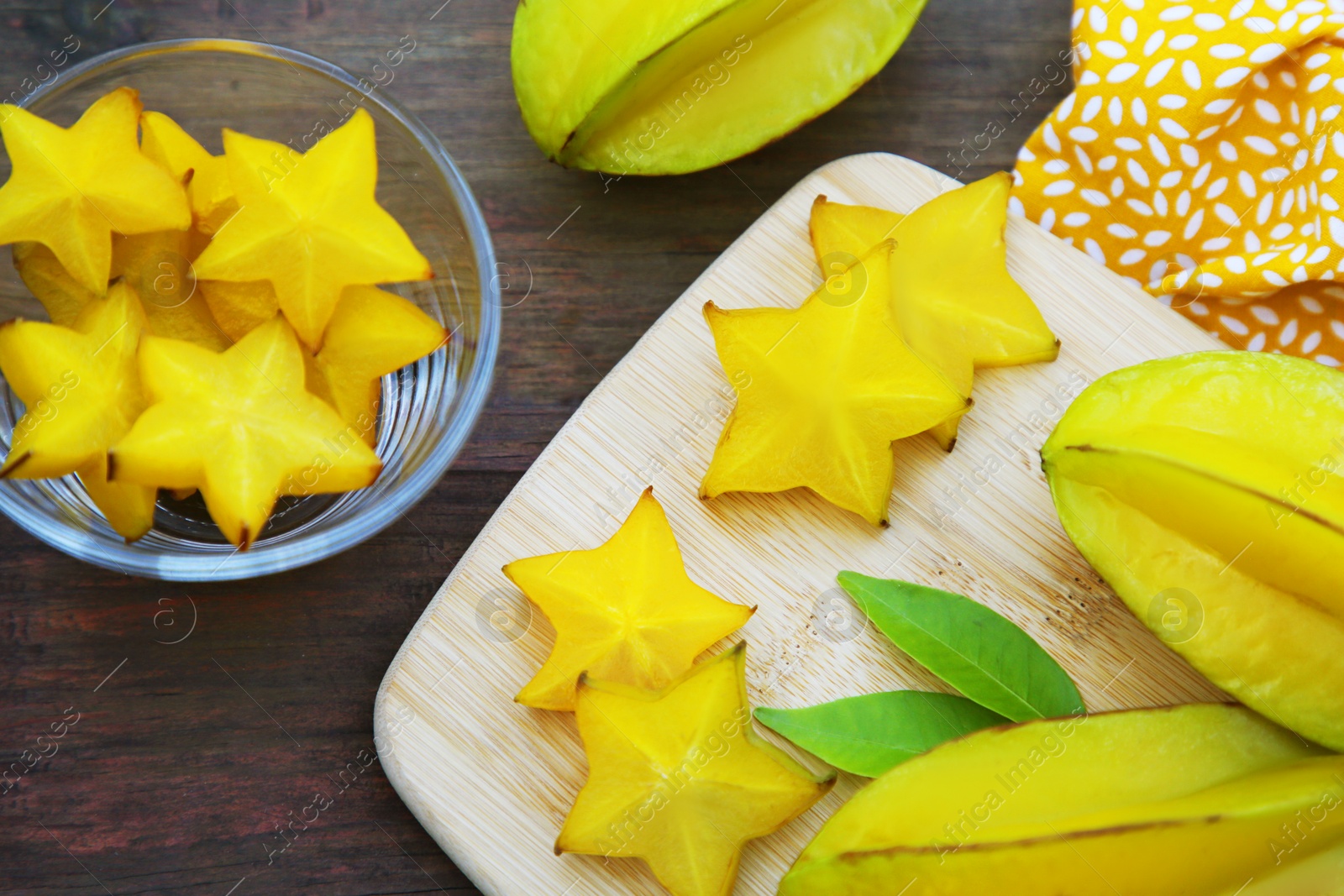 Photo of Delicious cut and whole carambolas with green leaves on wooden table, flat lay