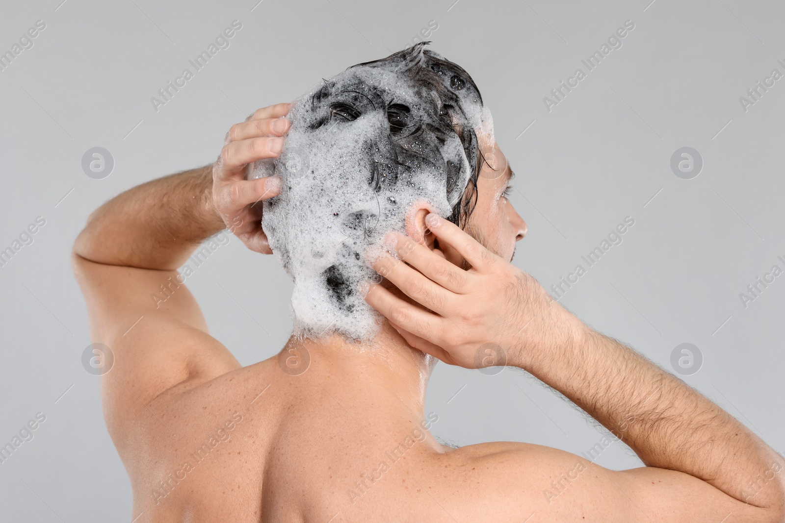 Photo of Man washing his hair with shampoo on grey background, back view