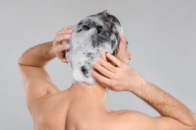 Man washing his hair with shampoo on grey background, back view