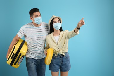 Photo of Couple of tourists in medical masks on light blue background. Travelling during coronavirus pandemic