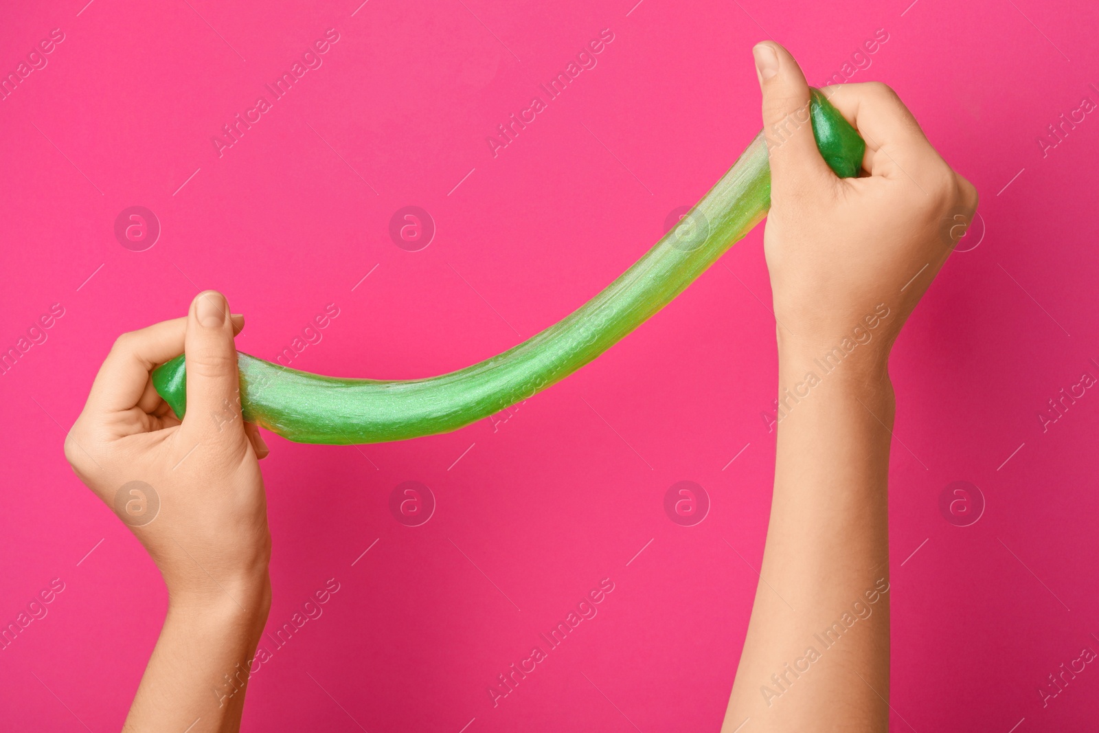 Photo of Woman playing with green slime on pink background, closeup. Antistress toy