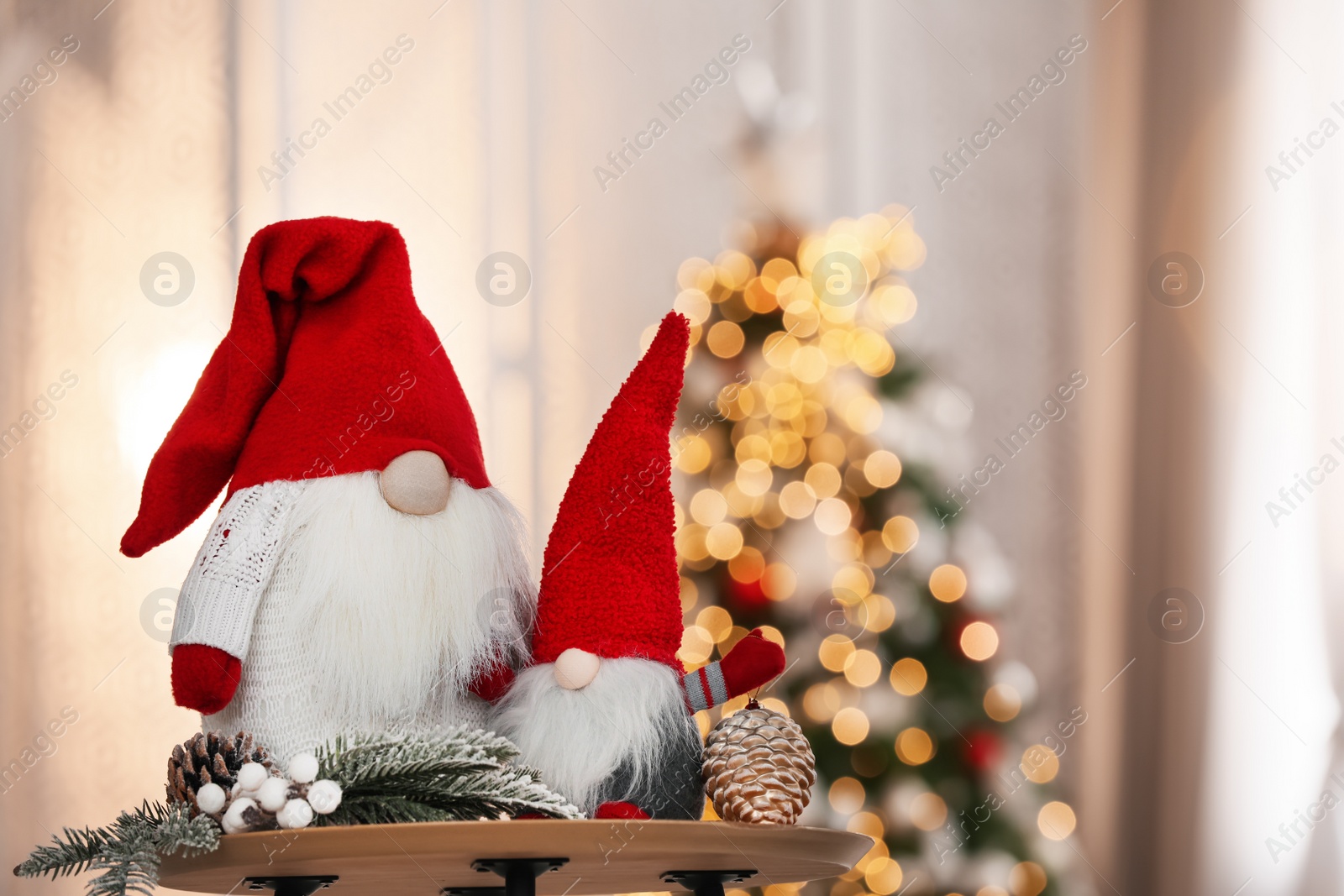 Photo of Cute Christmas gnomes on wooden table in decorated room, space for text
