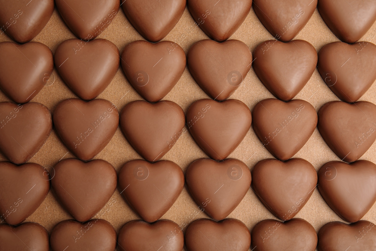 Photo of Tasty heart shaped chocolate candies on brown background, flat lay. Valentine's day celebration