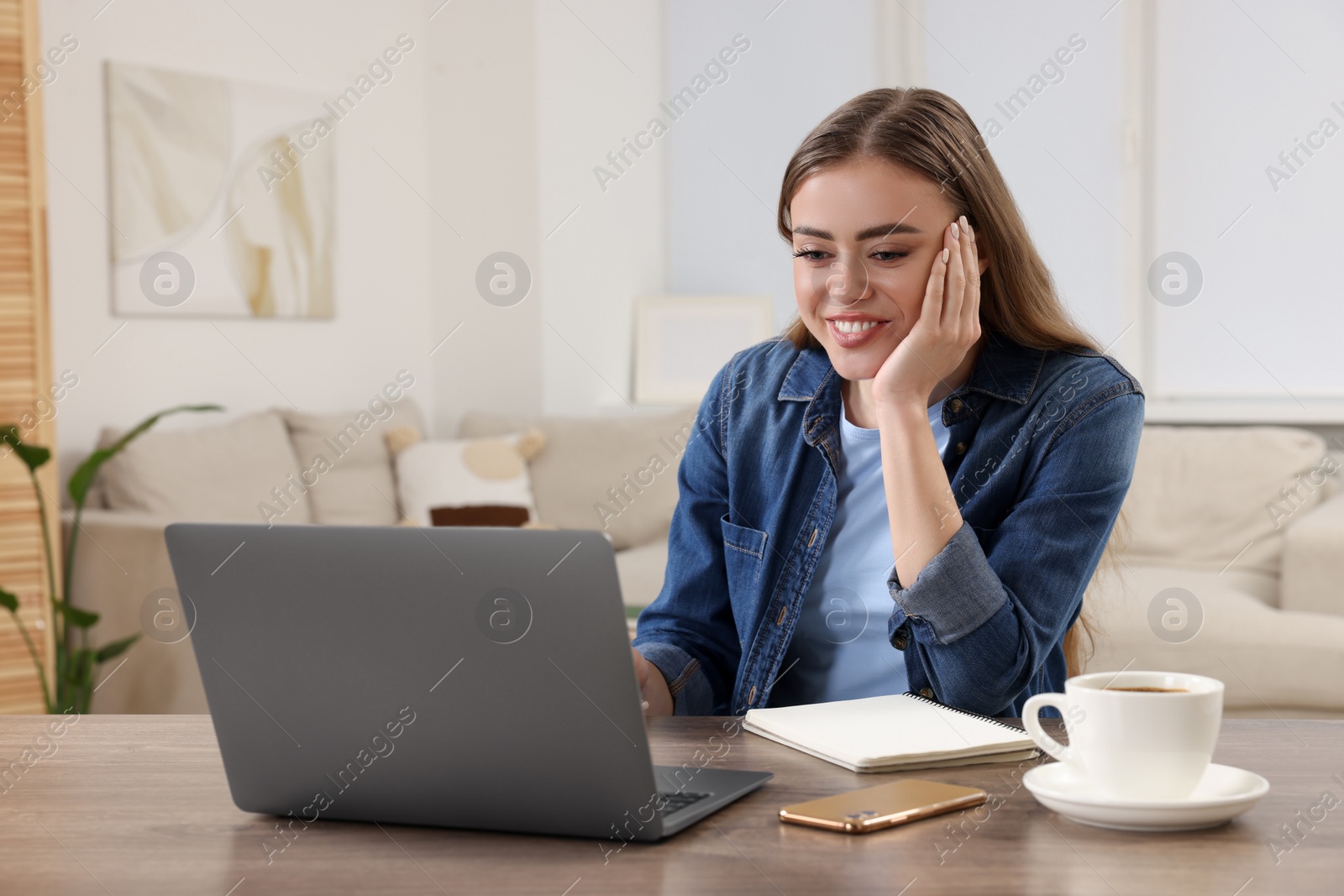 Photo of Happy woman with laptop at wooden table in room