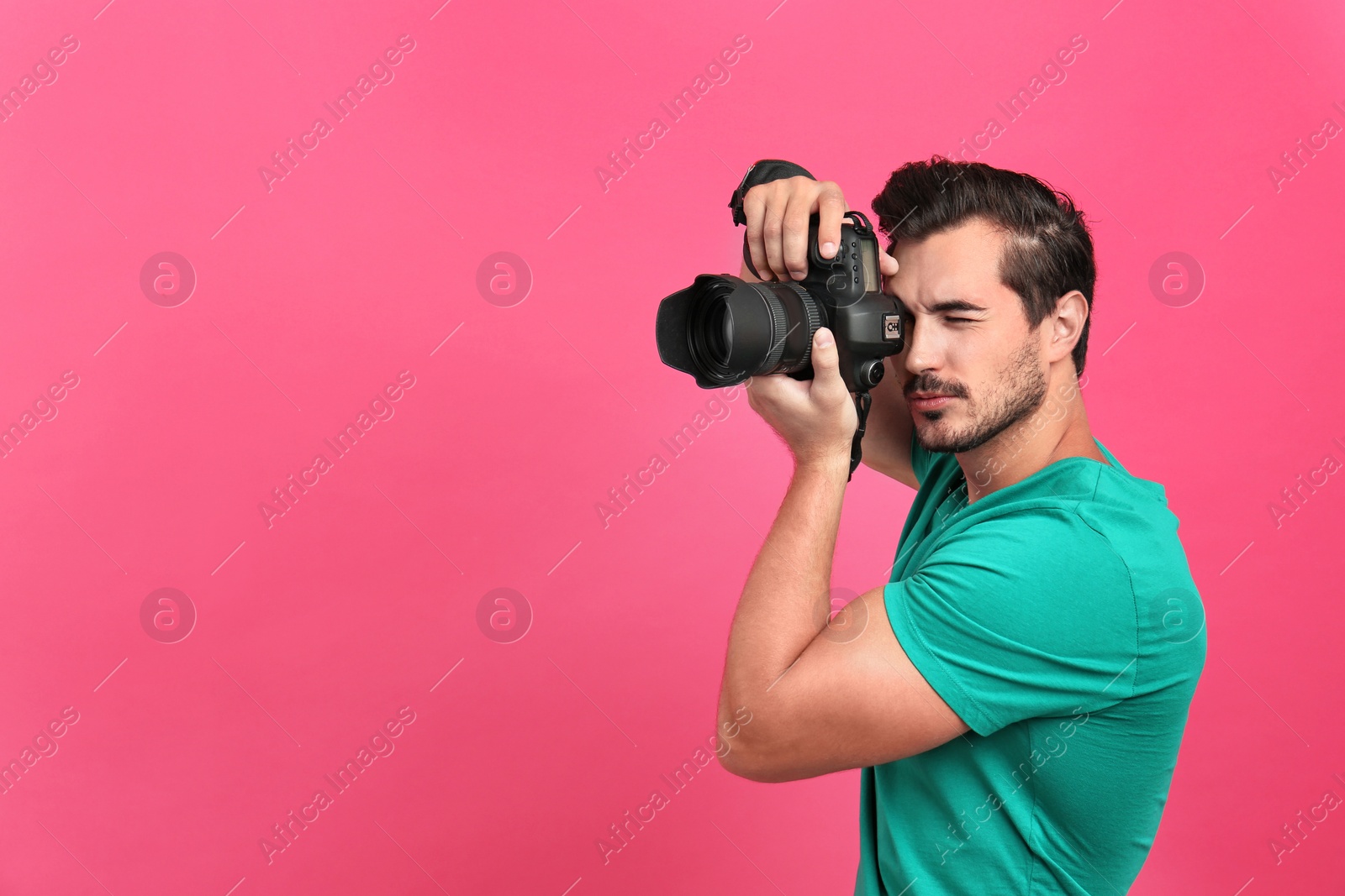 Photo of Young professional photographer taking picture on pink background. Space for text