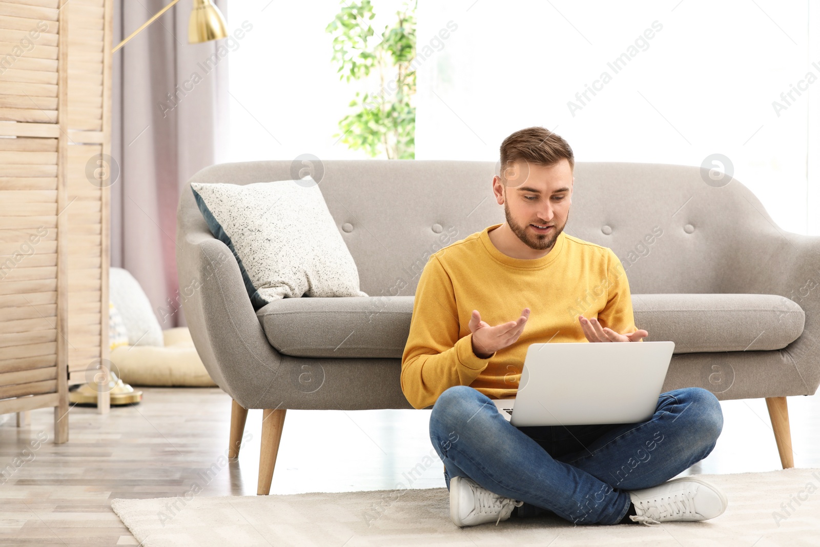 Photo of Young man using video chat on laptop in living room