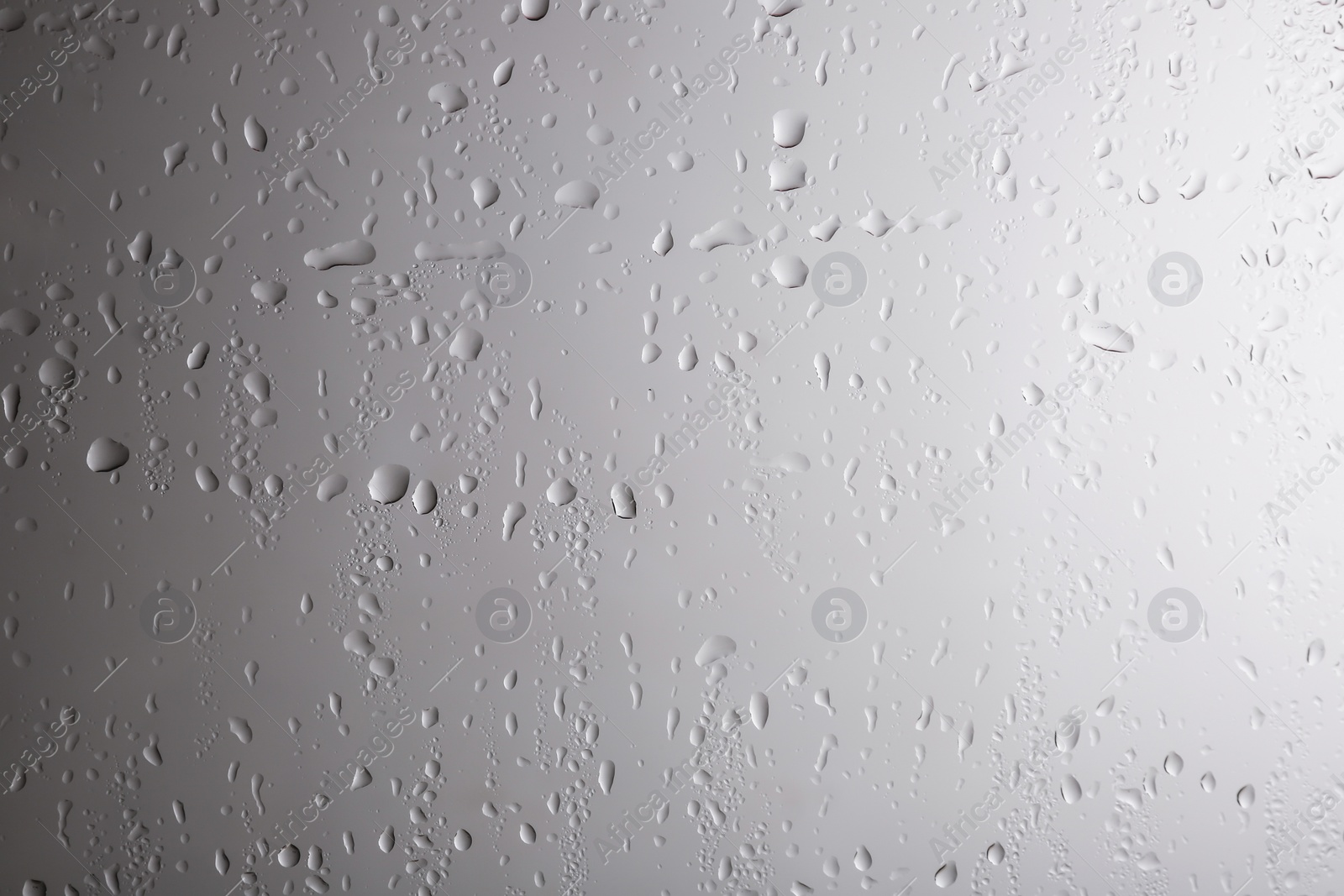 Photo of Glass with rain drops against light background