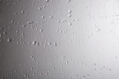 Photo of Glass with rain drops against light background