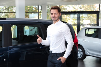 Photo of Young man near new car in dealership