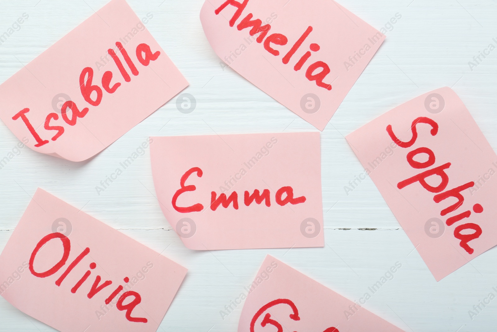 Photo of Paper stickers with different names on white wooden background, flat lay. Choosing baby's name