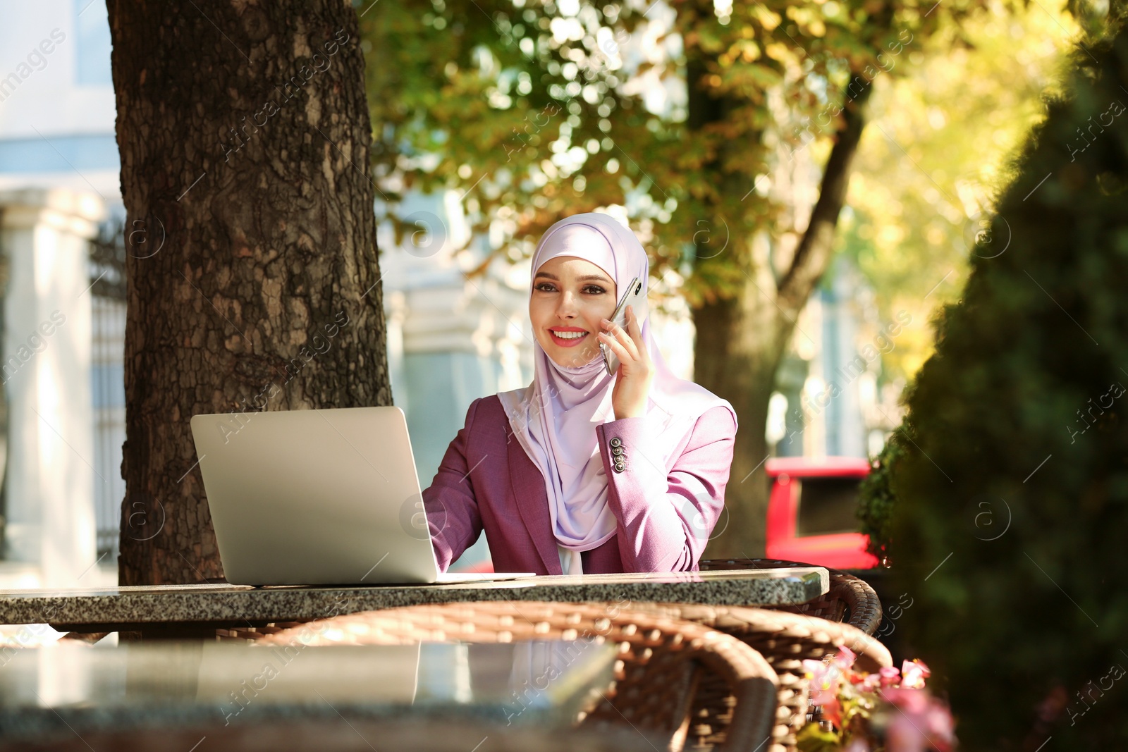 Photo of Muslim woman talking on phone in outdoor cafe