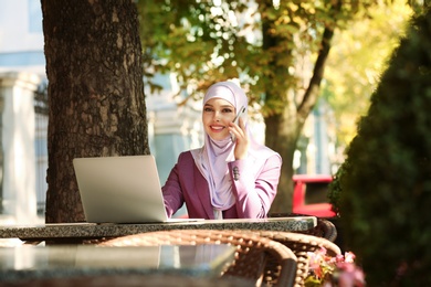 Muslim woman talking on phone in outdoor cafe