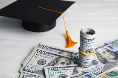 Photo of Dollar banknotes and student graduation hat on white wooden background. Tuition fees concept