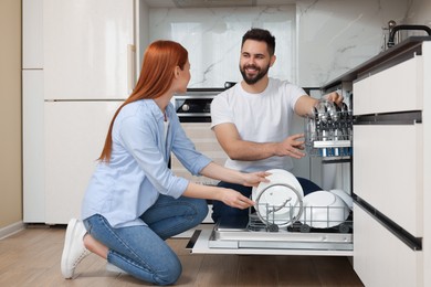 Photo of Happy couple loading dishwasher with plates in kitchen