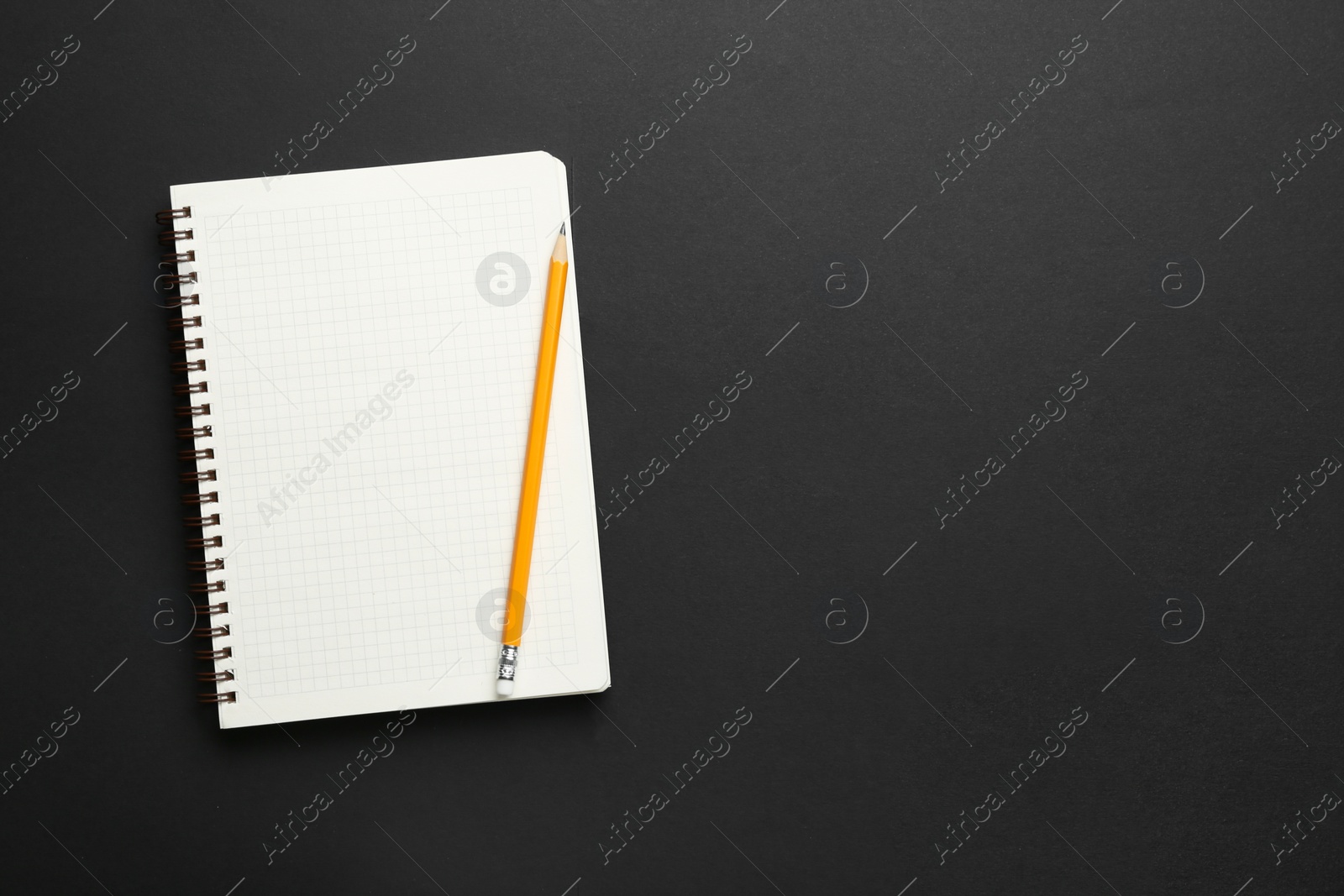 Photo of Notebook and pencil on black background, top view. Space for text