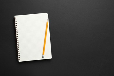 Photo of Notebook and pencil on black background, top view. Space for text