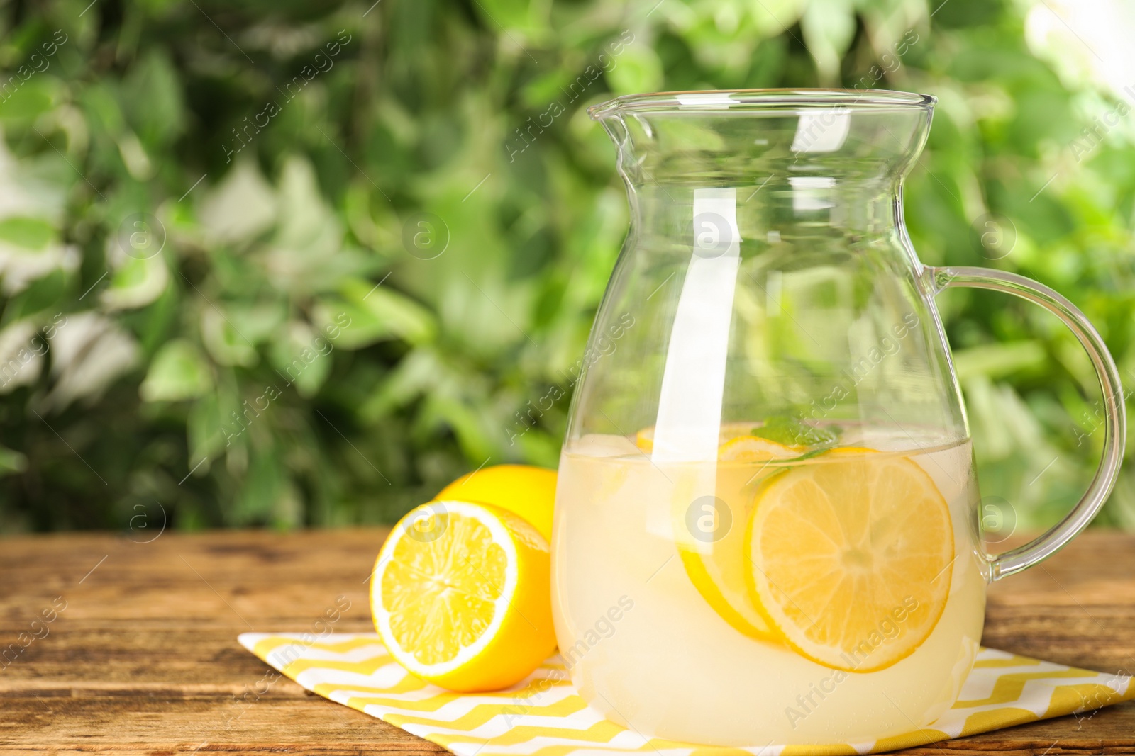 Photo of Cool freshly made lemonade in glass pitcher on wooden table. Space for text