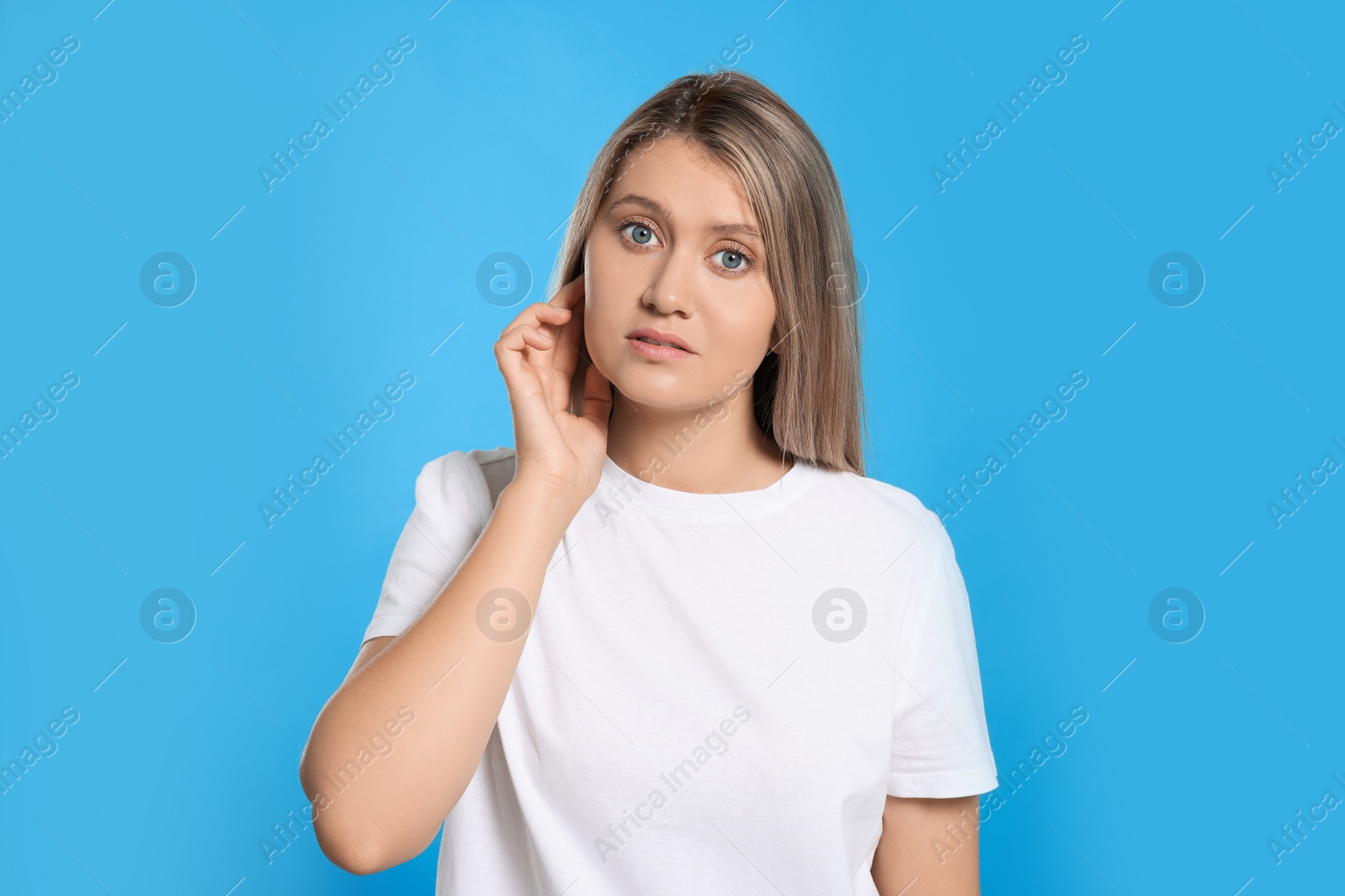 Photo of Young woman suffering from ear pain on light blue background