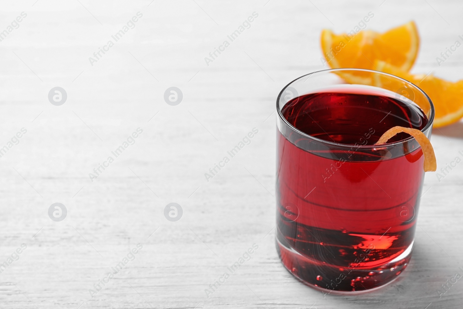 Photo of Glass of tasty refreshing cocktail with orange peel on while wooden table. Space for text