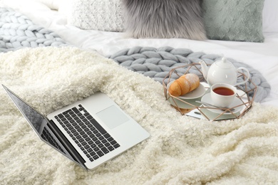 Tray with tasty breakfast and laptop on bed