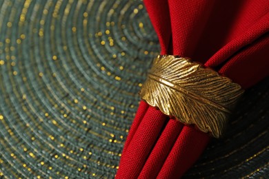Photo of Red fabric napkin and decorative ring on serving mat, closeup. Space for text