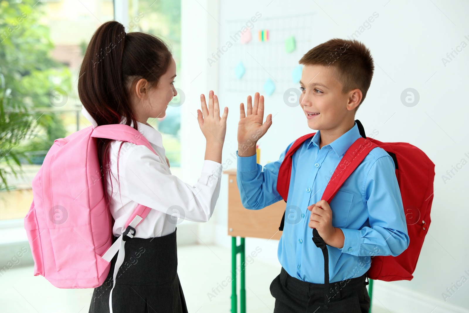 Photo of Cute little girl giving boy high five in classroom at school