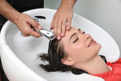 Photo of Professional hairdresser washing client's hair at sink indoors, closeup