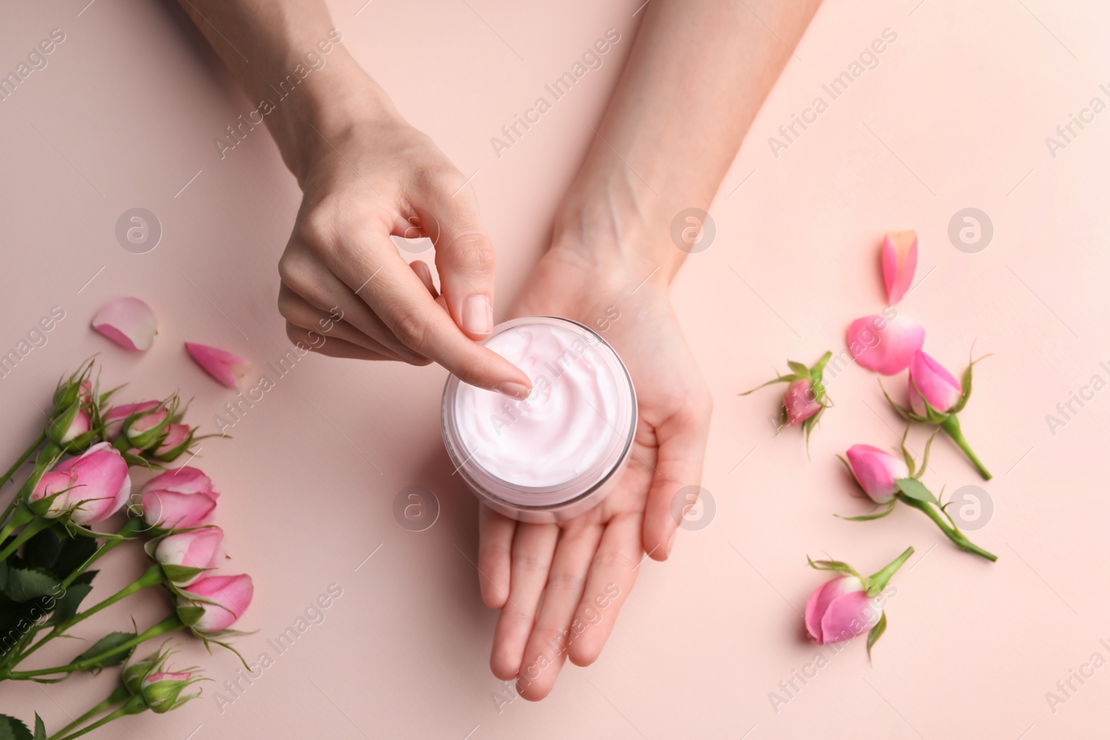 Photo of Woman holding jar of hand cream on pink background, top view