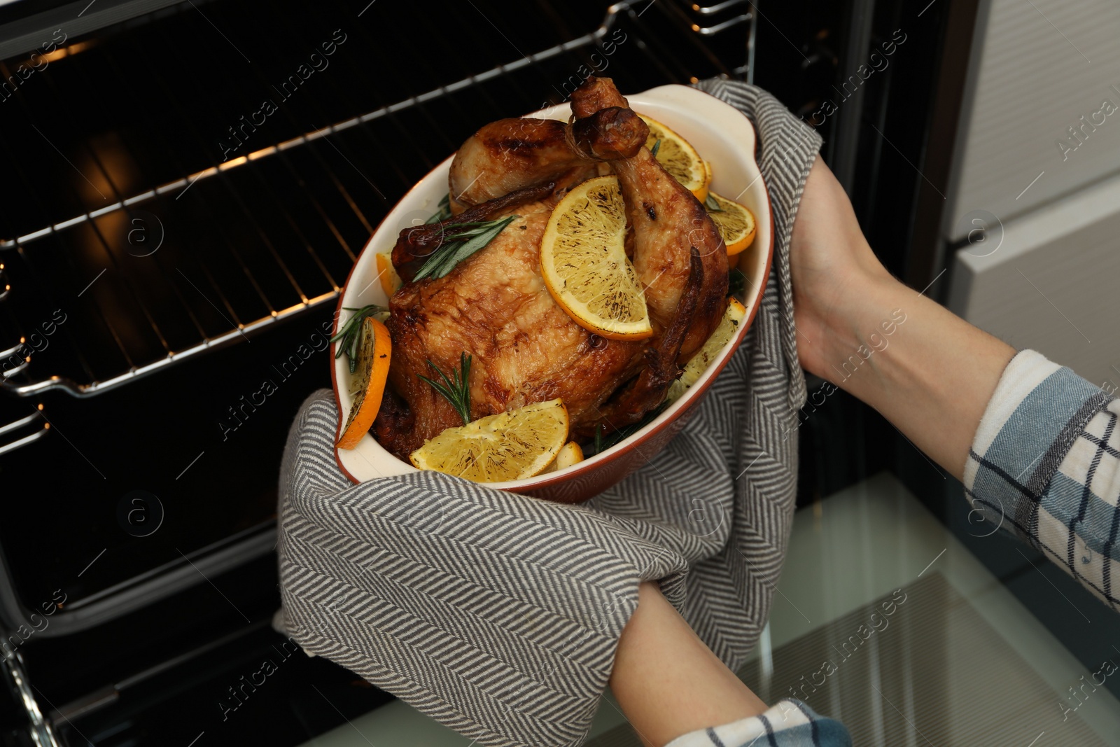 Photo of Woman taking baked chicken with orange slices out of oven, closeup