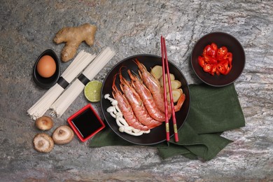 Cooking delicious ramen soup. Different ingredients and chopsticks on gray textured table, flat lay