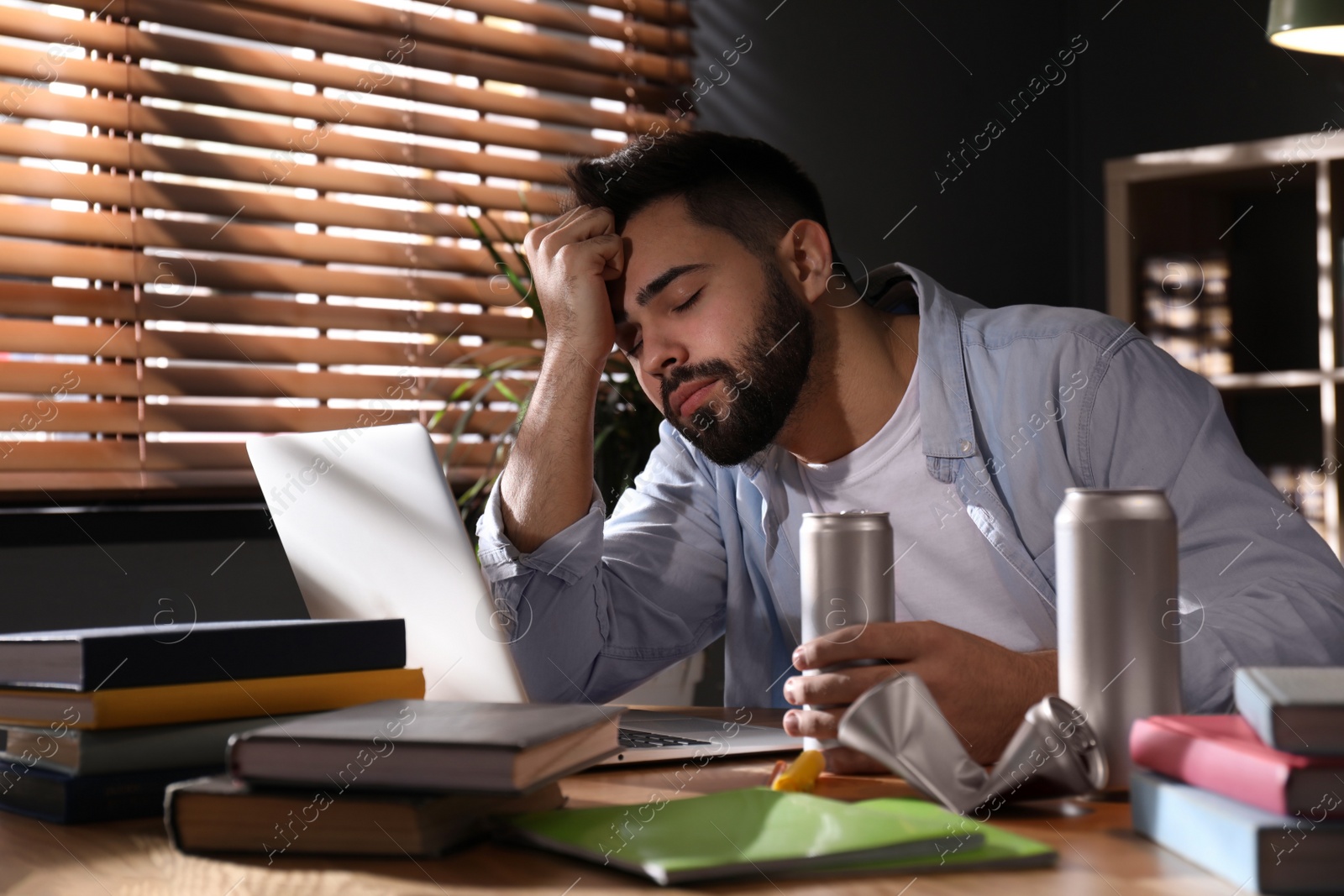 Photo of Tired young man with energy drink studying at home